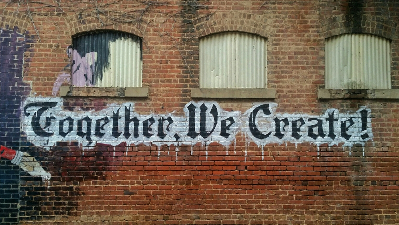 Brick wall with graffiti text 'Together, We Create'.