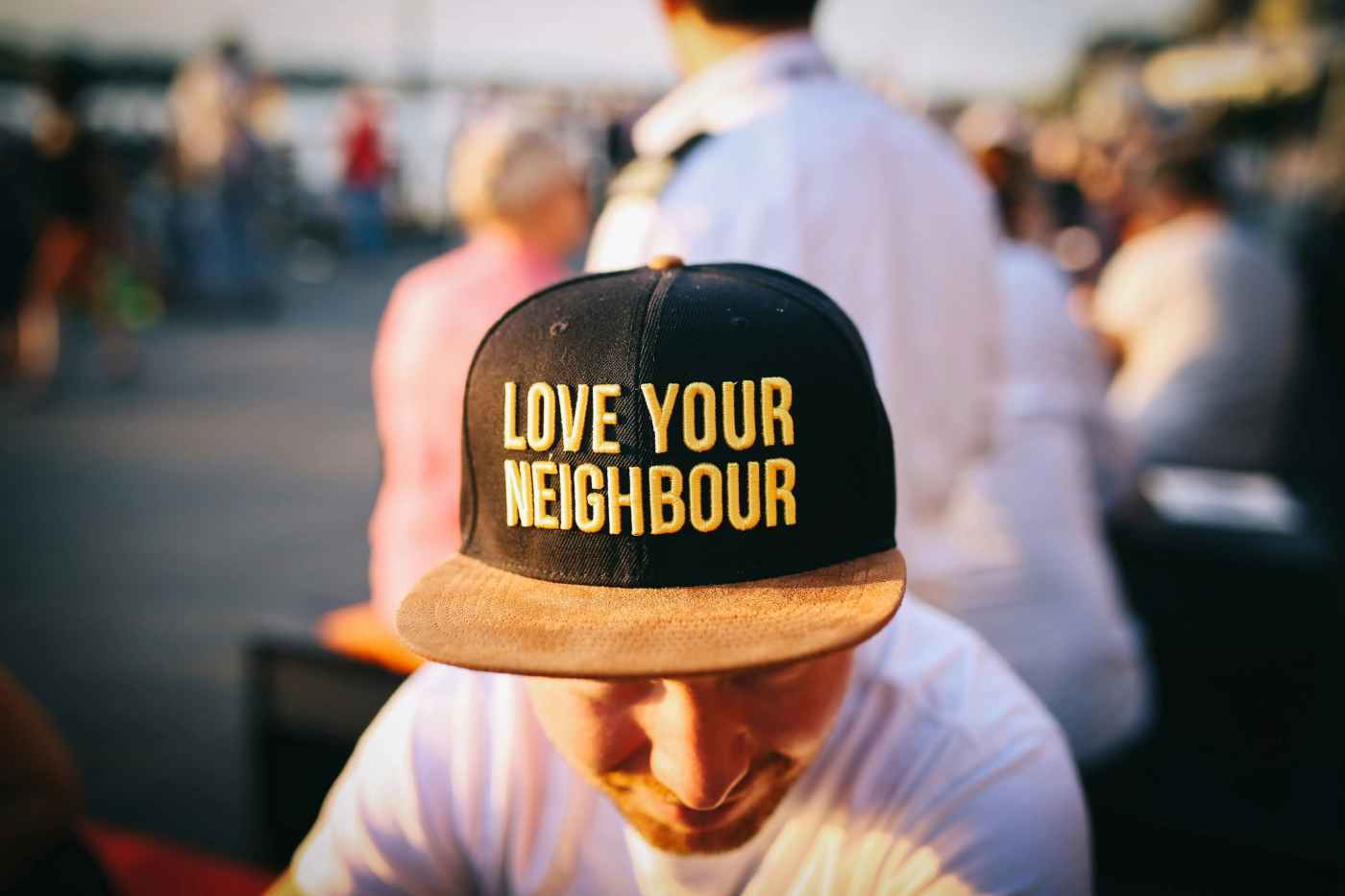 Cap with the message 'LOVE YOUR NEIGHBOUR' worn at a sunny outdoor event.