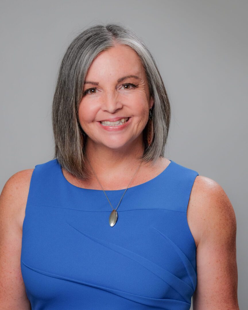 Smiling woman with gray hair wearing a blue sleeveless dress.