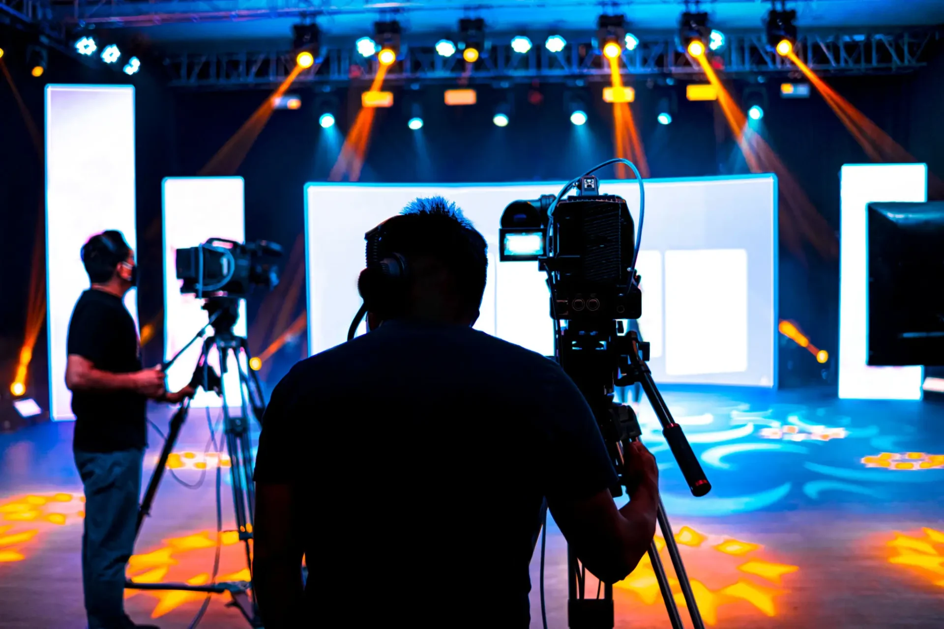 Silhouette of a cameraman filming on a brightly lit stage with colorful lights.